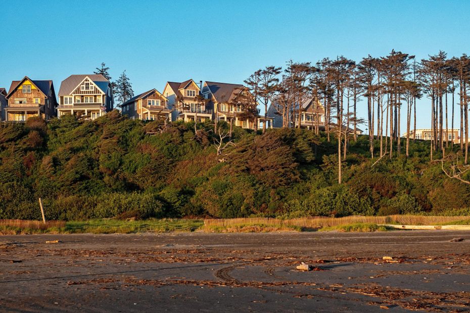 Seaside homes sit atop a cliff at sunset, surrounded by evergreen trees at Seabrook, Washington State.