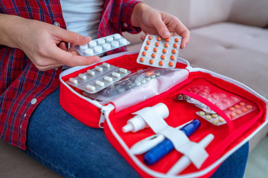 A woman puts medications into a red first aid kit.