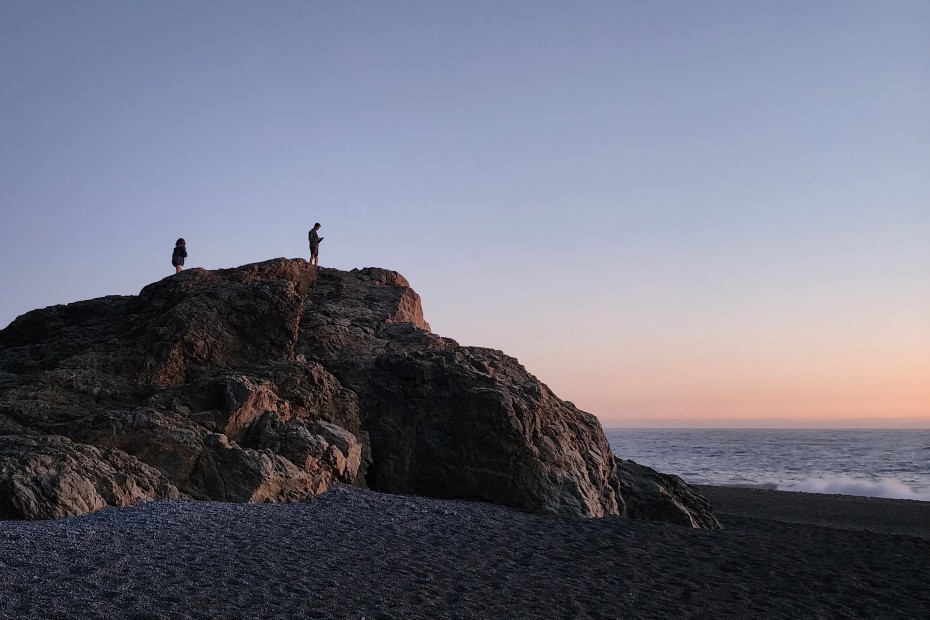 Two people stand on a large rock on California's Lost Coast at sunset.