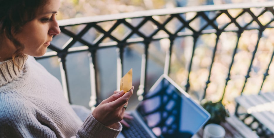 A woman looks at her credit card after getting a fraud alert on her laptop