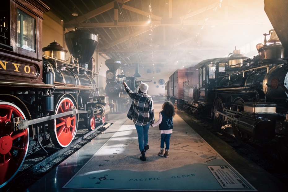 A mother and daughter walk between two train engines inside the Nevada State Railroad Museum.