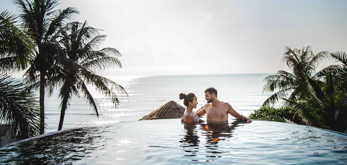 a happy couple in an infinity pool near palm trees at sunset