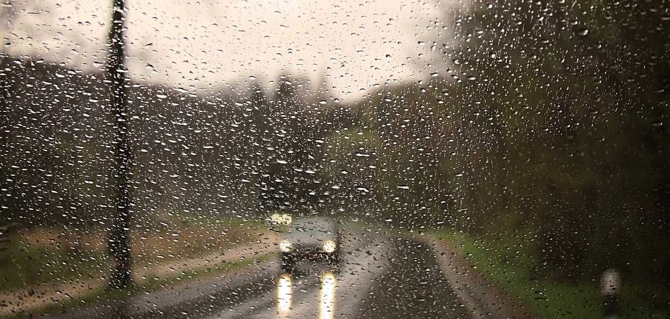 car driving on a wet road seen through a rainy windshield