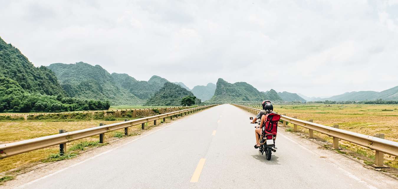 A backpacker couple rides through Vietnam on an antique motorcycle