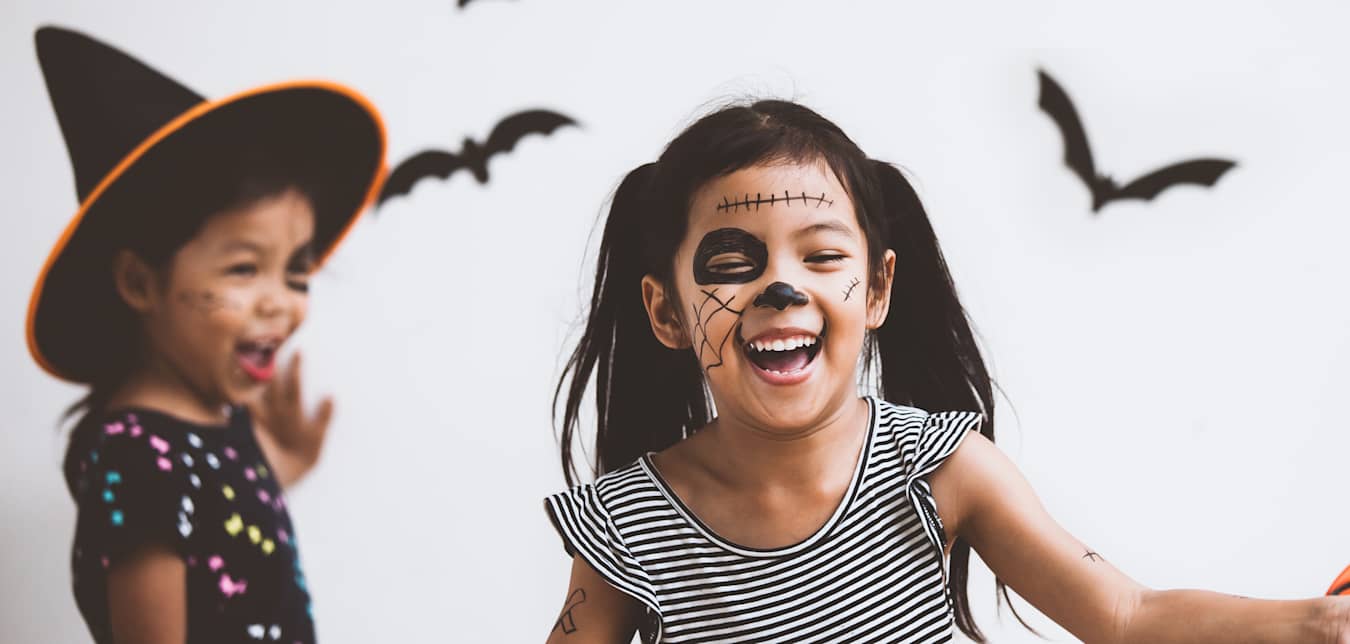 Two girls with face paint put up Halloween decorations bats