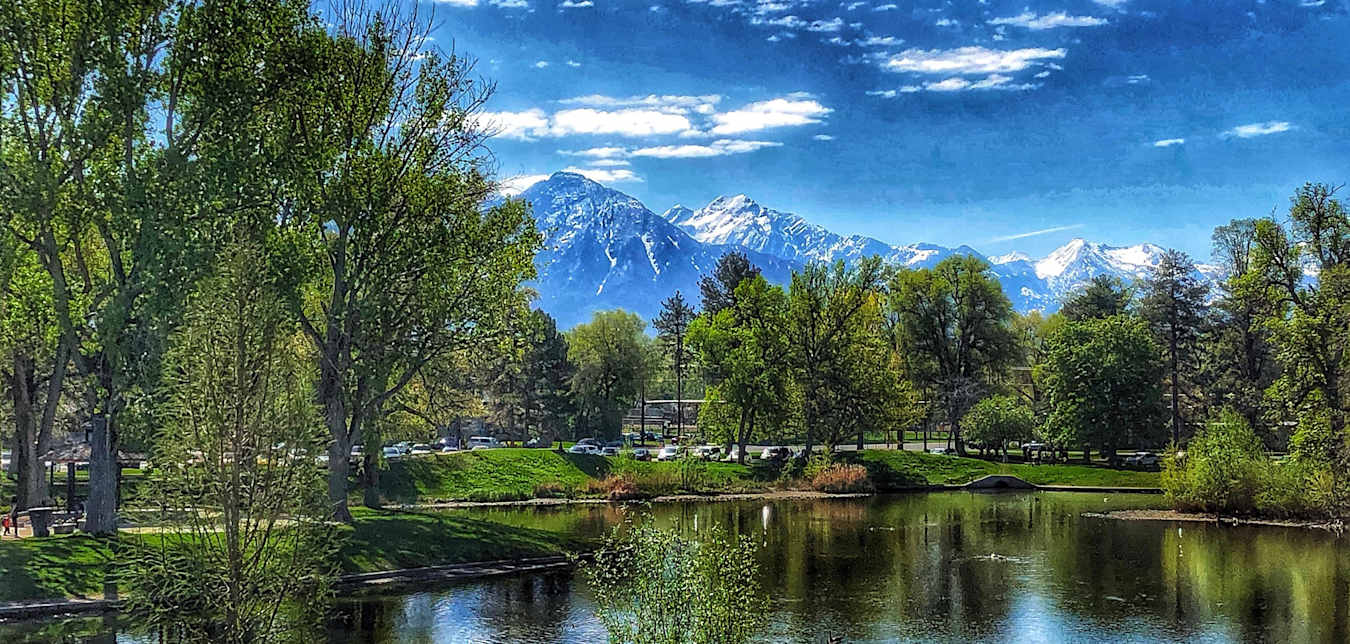 Liberty Lake surrounded by green, leafy trees under blue, partly cloudy sky at Liberty Park in Salt Lake City, Utah.