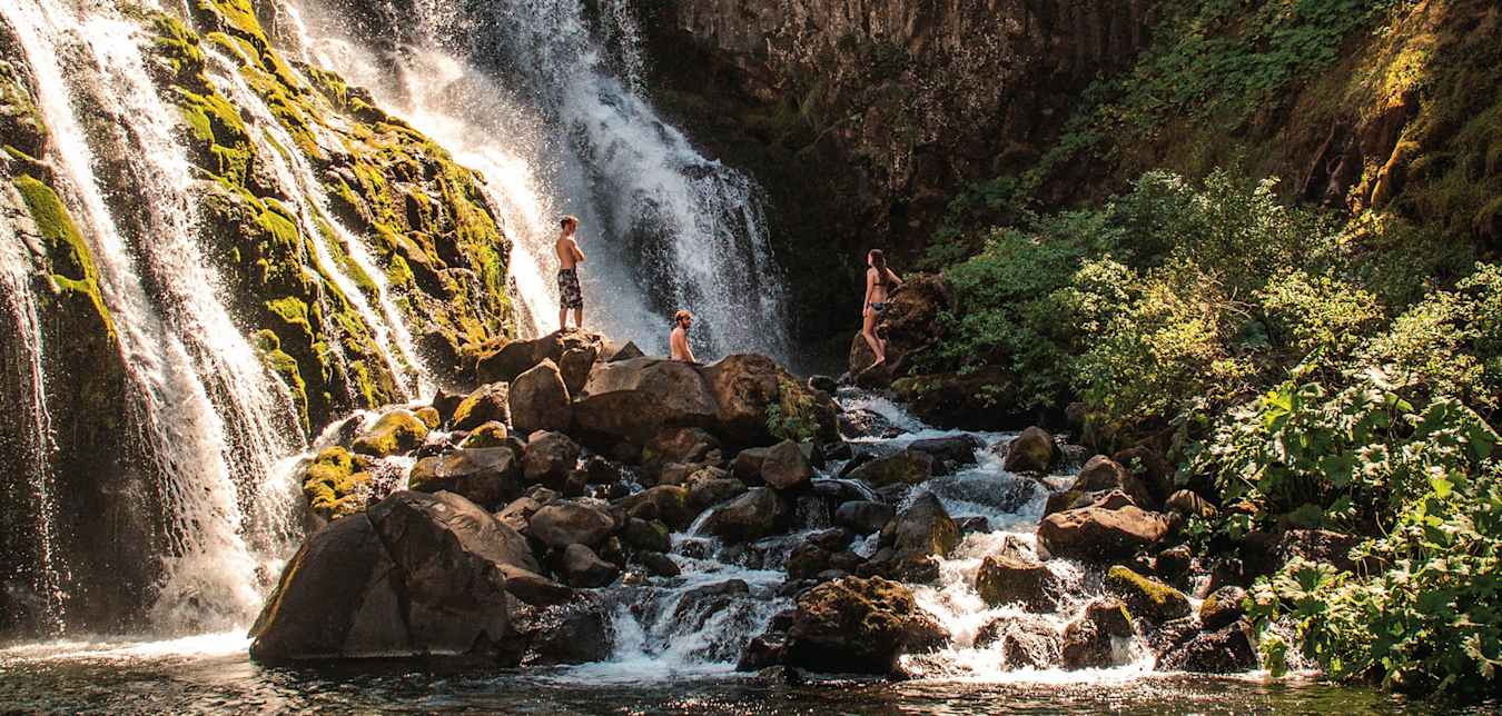 trio of swimmers admire Middle Falls from rocks below on the McCloud River near Mt Shasta, California
