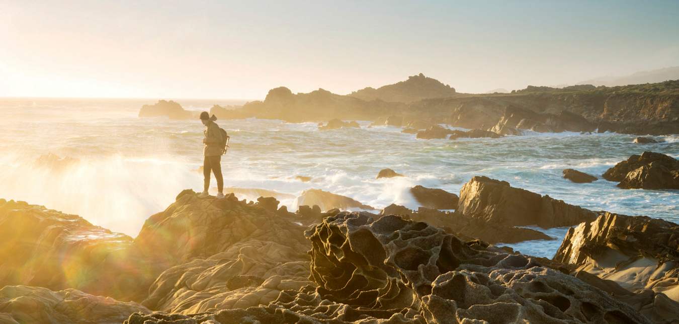 Hiker dressed warmly and standing on the honeycombed rocks known as tafoni looks out to sea at sunset at Salt Point State Park on the Sonoma Coast in California