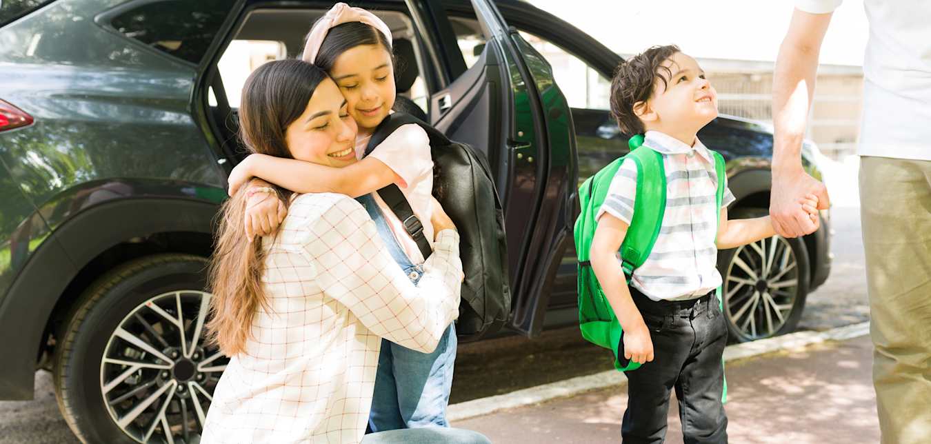 A mom hugs her daughter at school drop-off.