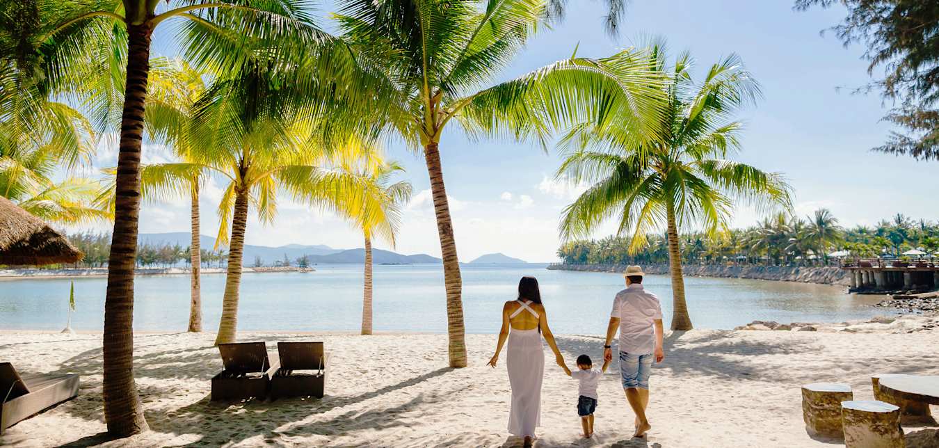 A family walks together on a white sand tropical beach.