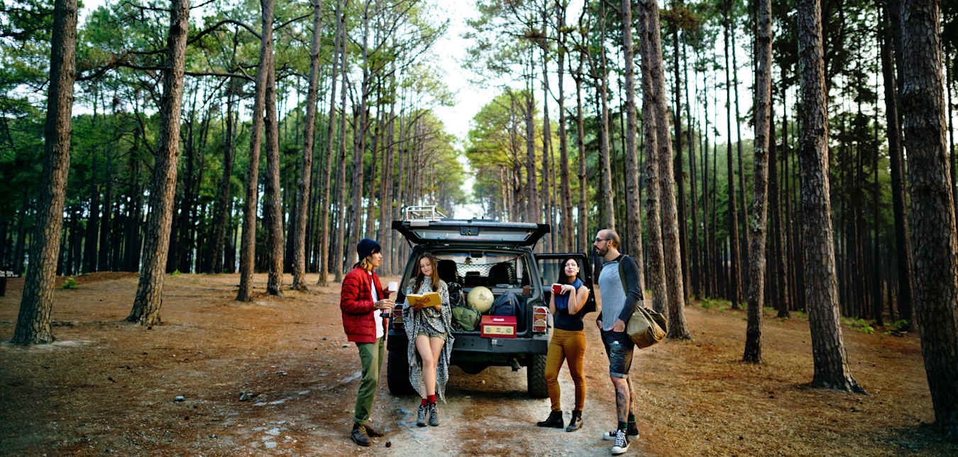 Friends stand around an open car tailgate with camping gear in the back