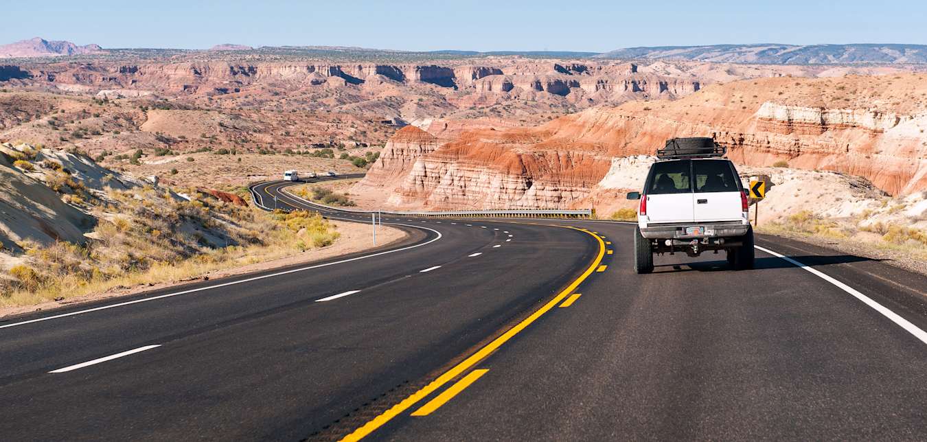A white SUV drives through the Arizona desert on a sunny day.