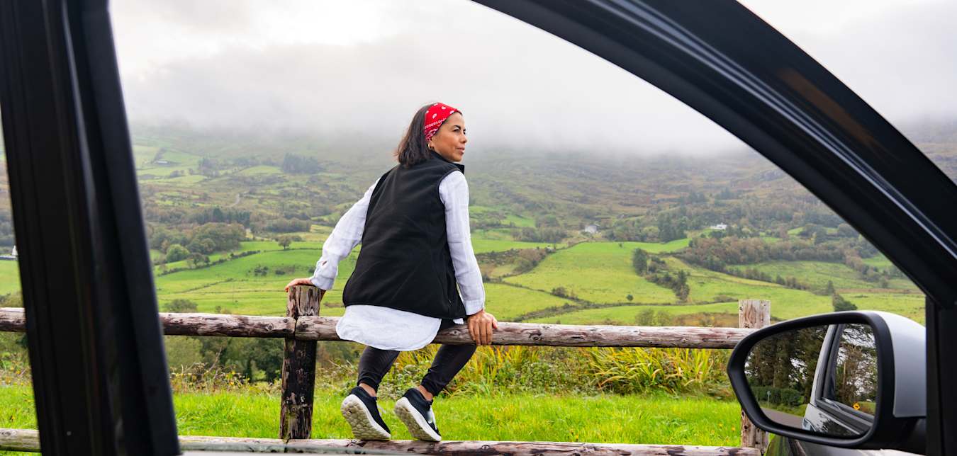 A woman sits on a fence beside her rental car in Spain.