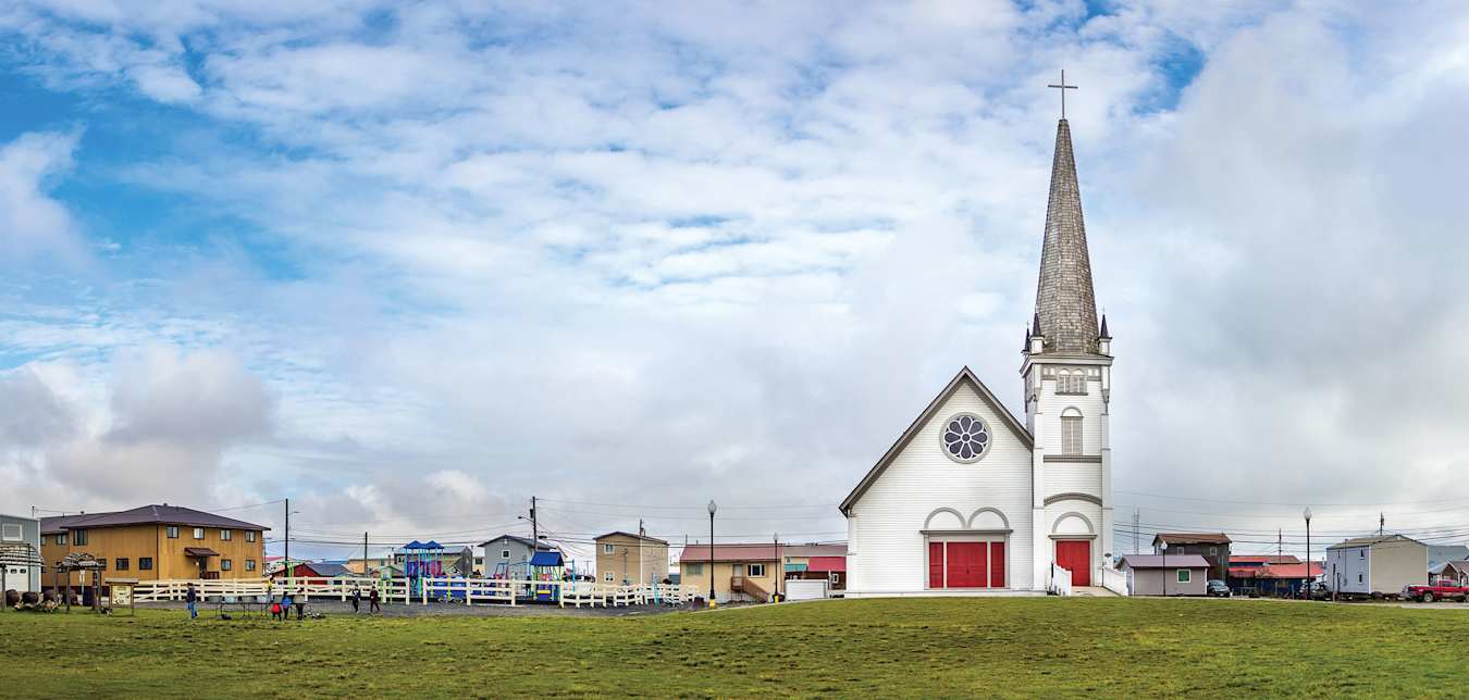 A photo of a city square with a church building, green grass and blue sky