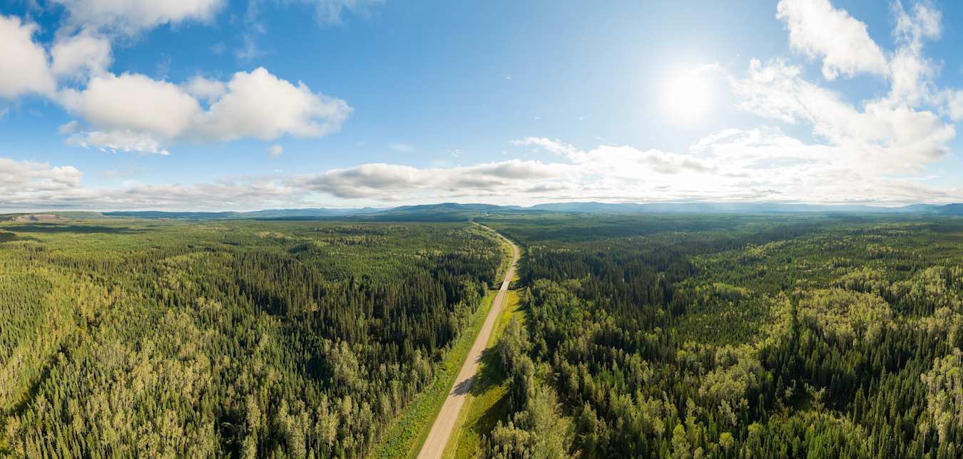 A highway cuts through green forests with blue skies above