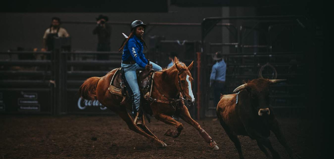 A female cattle roper on a horse on the Black rodeo circuit. 