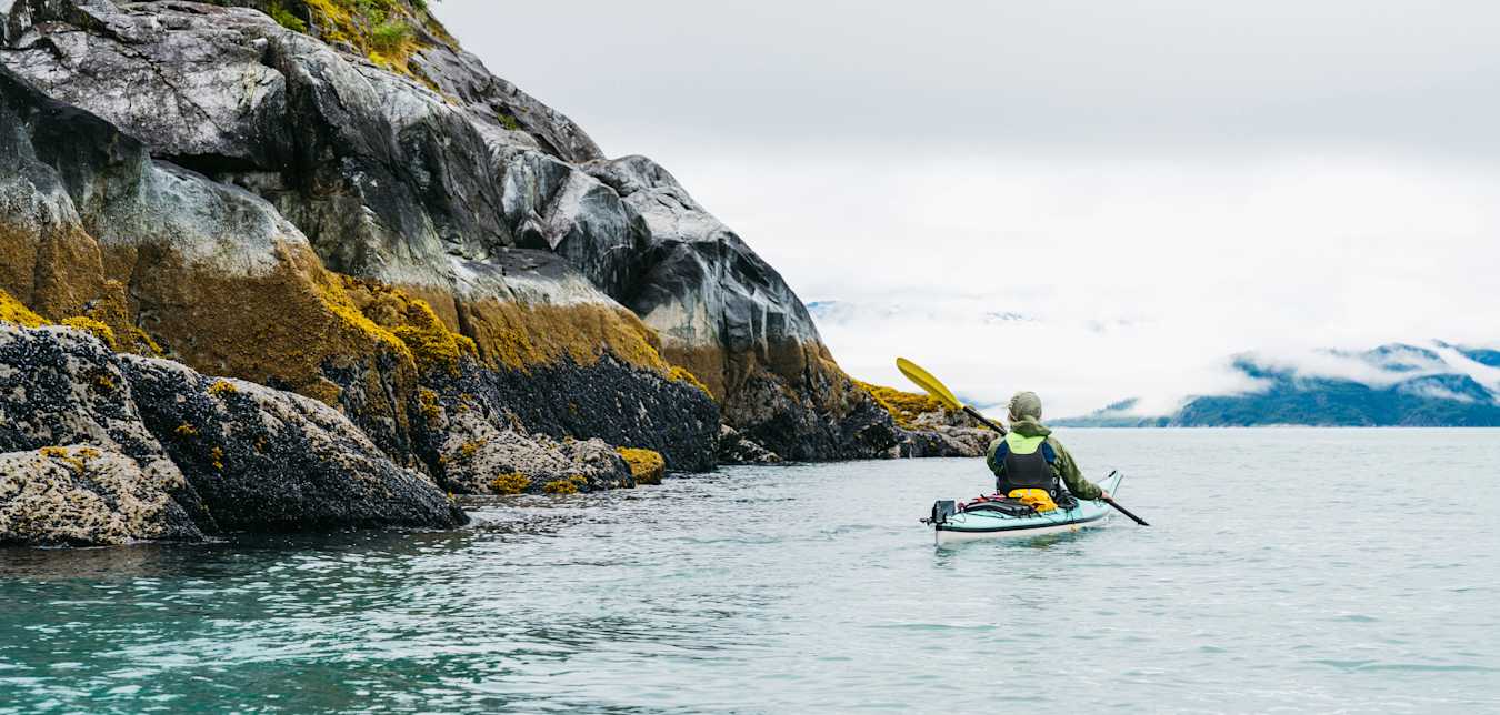 a person kayaks next to a picturesque mountain in Alaska