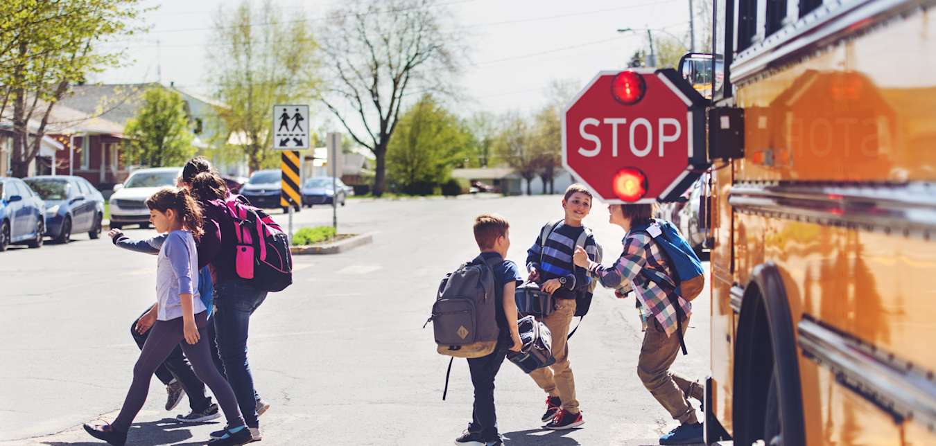 Kids with backpacks step off a school bus