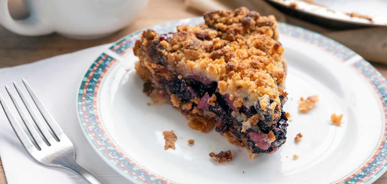 a piece of berry crumble pie on a white plate.