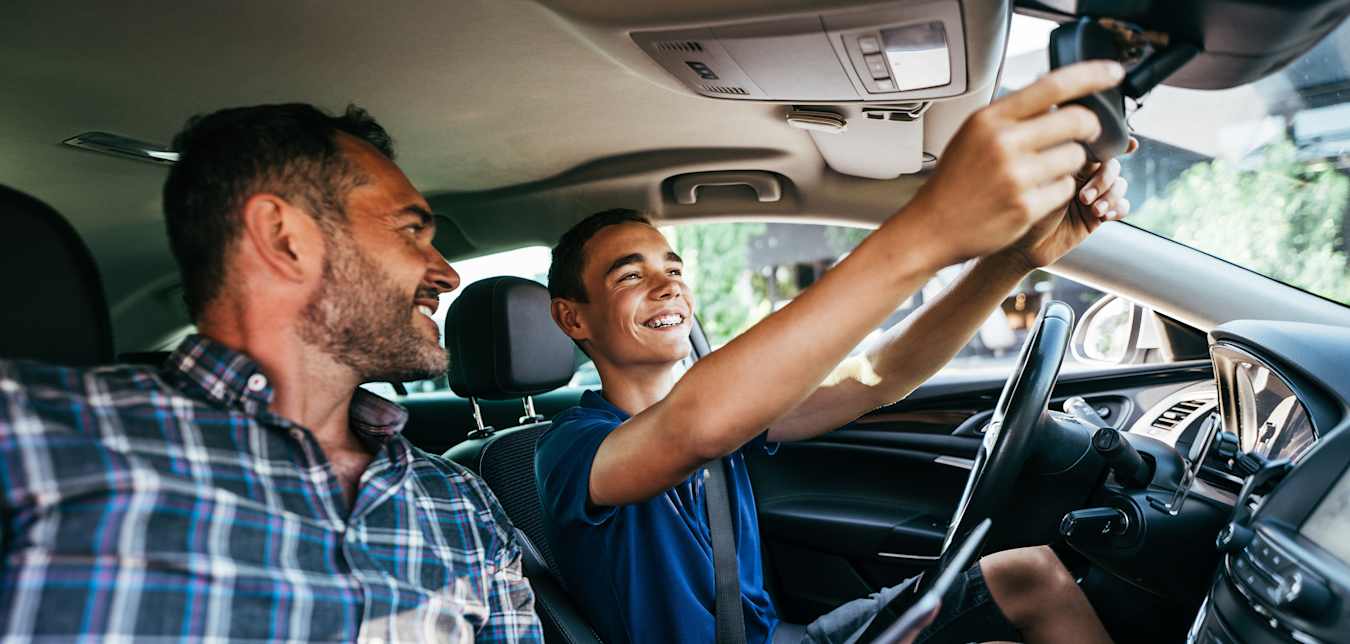 A teenager adjusts the mirrors in his parent's car before learning how to drive.