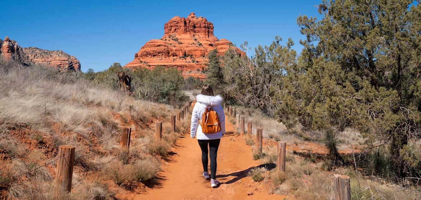 A person in a white coat walks on the Bell Rock Pathway in Sedona, Arizona.