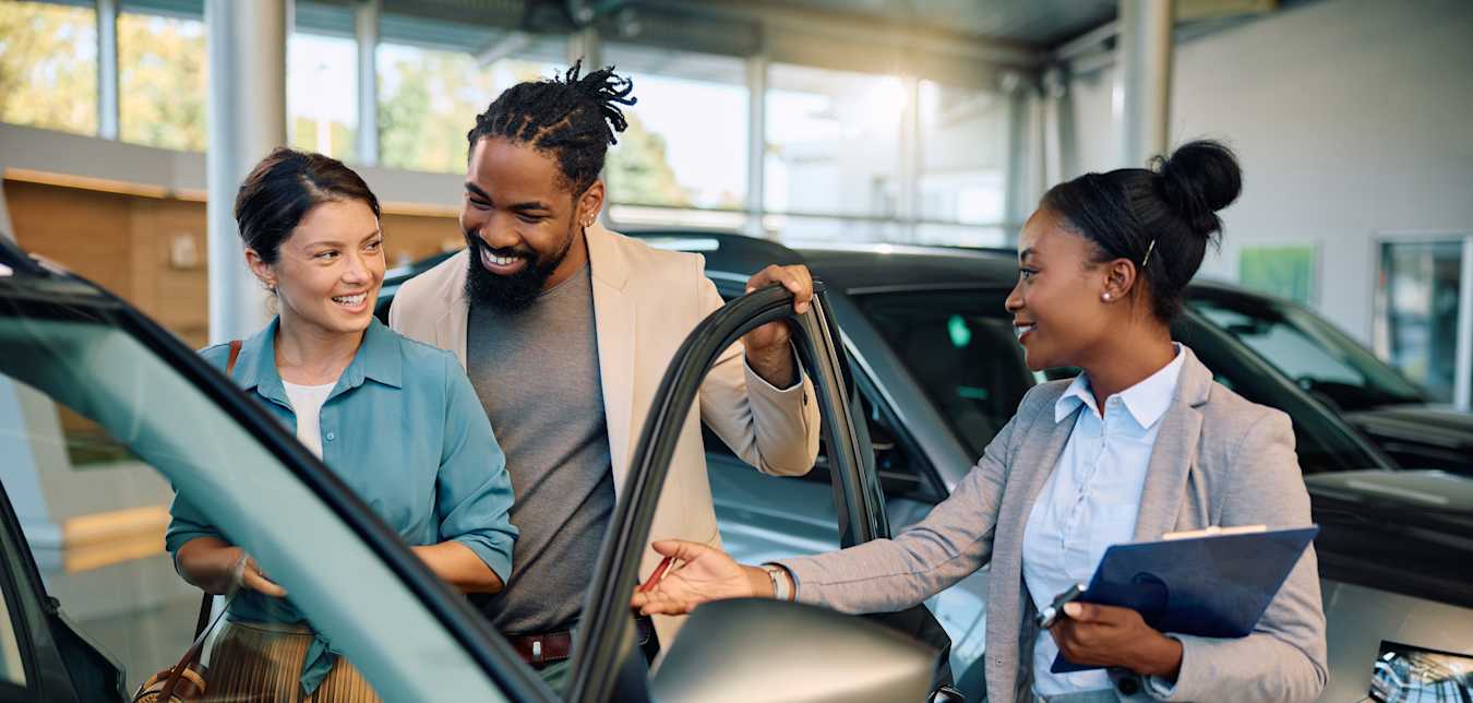 A couple look at new cars in a dealership showroom.