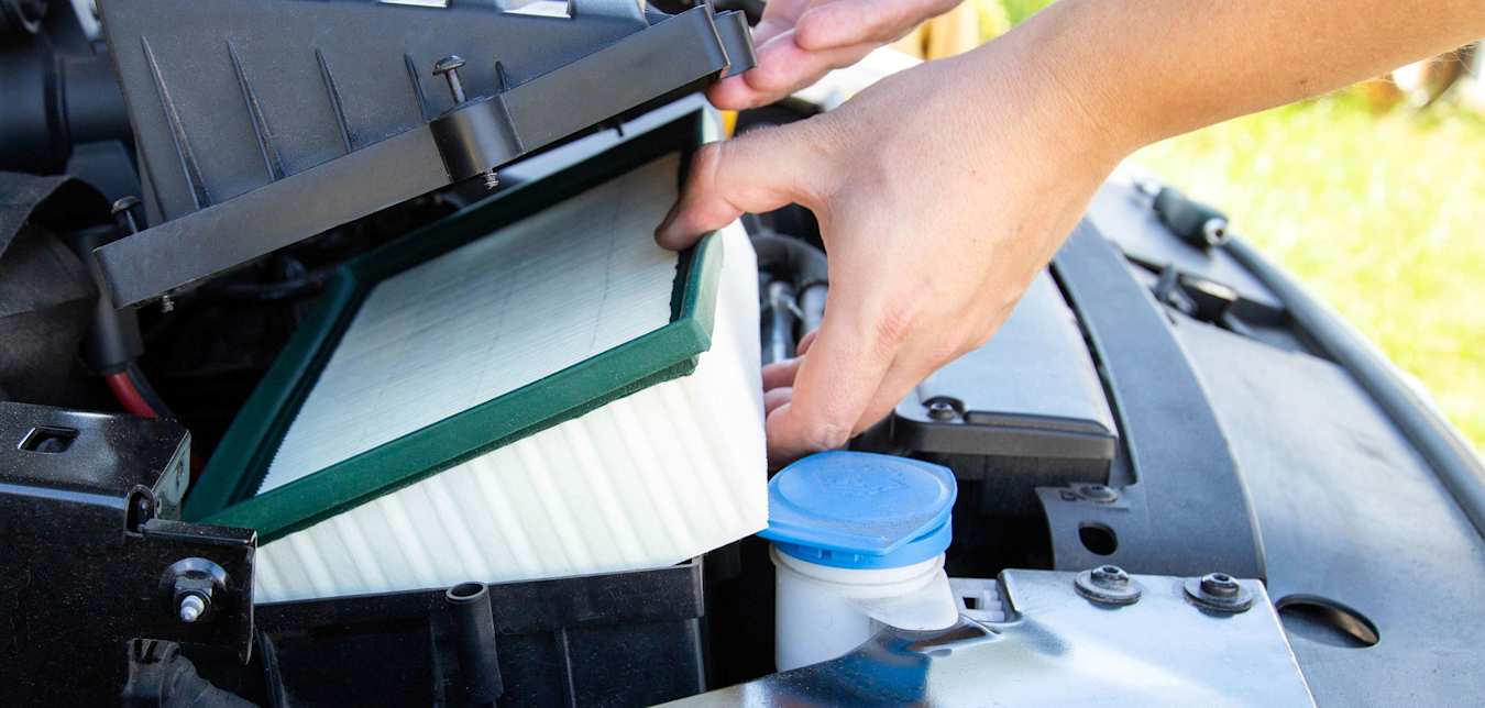 A person replaces their car engine air filter.