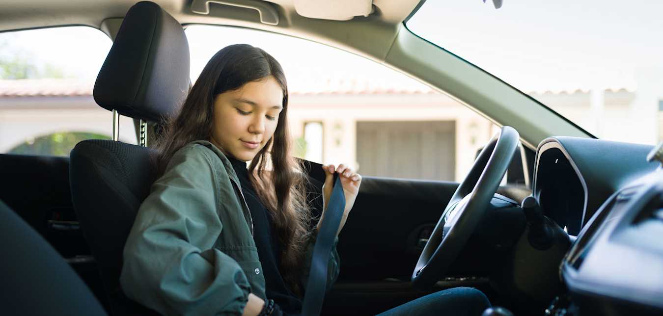 A teen puts on her setbelt before driving on a sunny day.