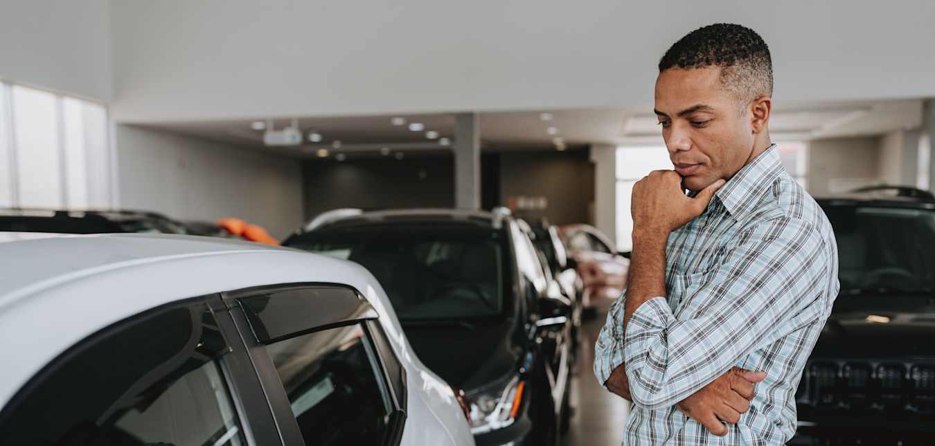 A man looks at a white sedan in a dealership showroom.