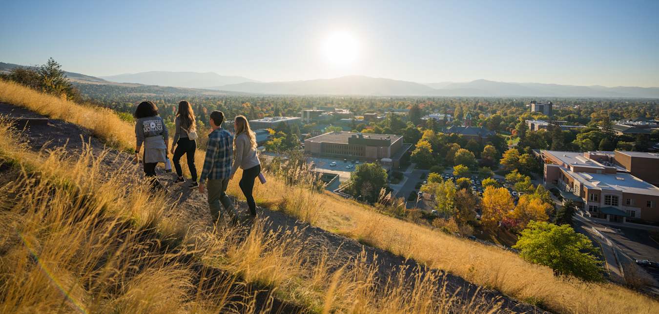 four people hike up a mountain with dry grass and a view of Missoula, Montana