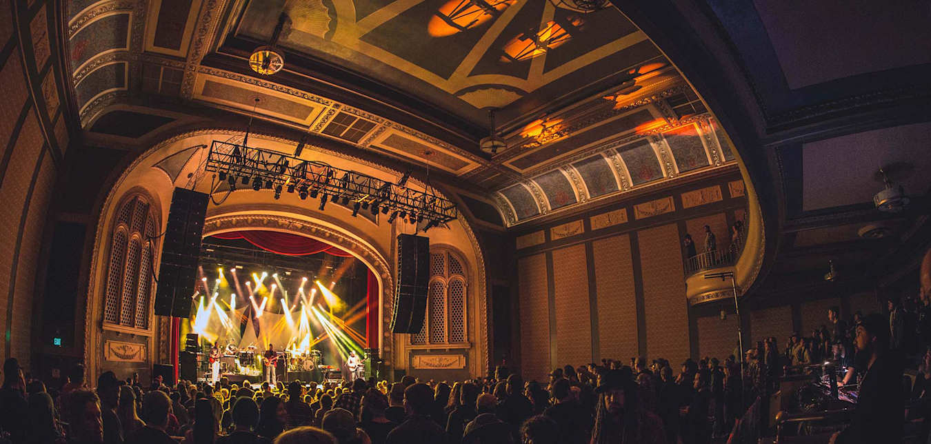 a packed concert hall with an ornate ceiling