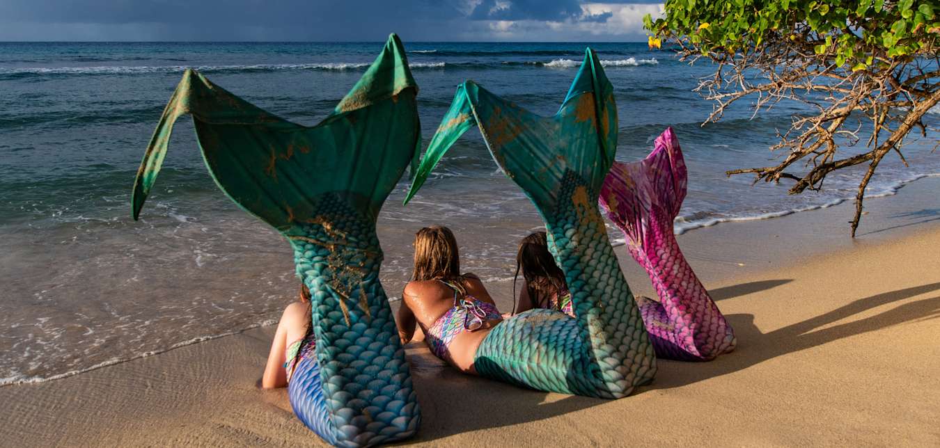 Mermaids lounge on a beach together.