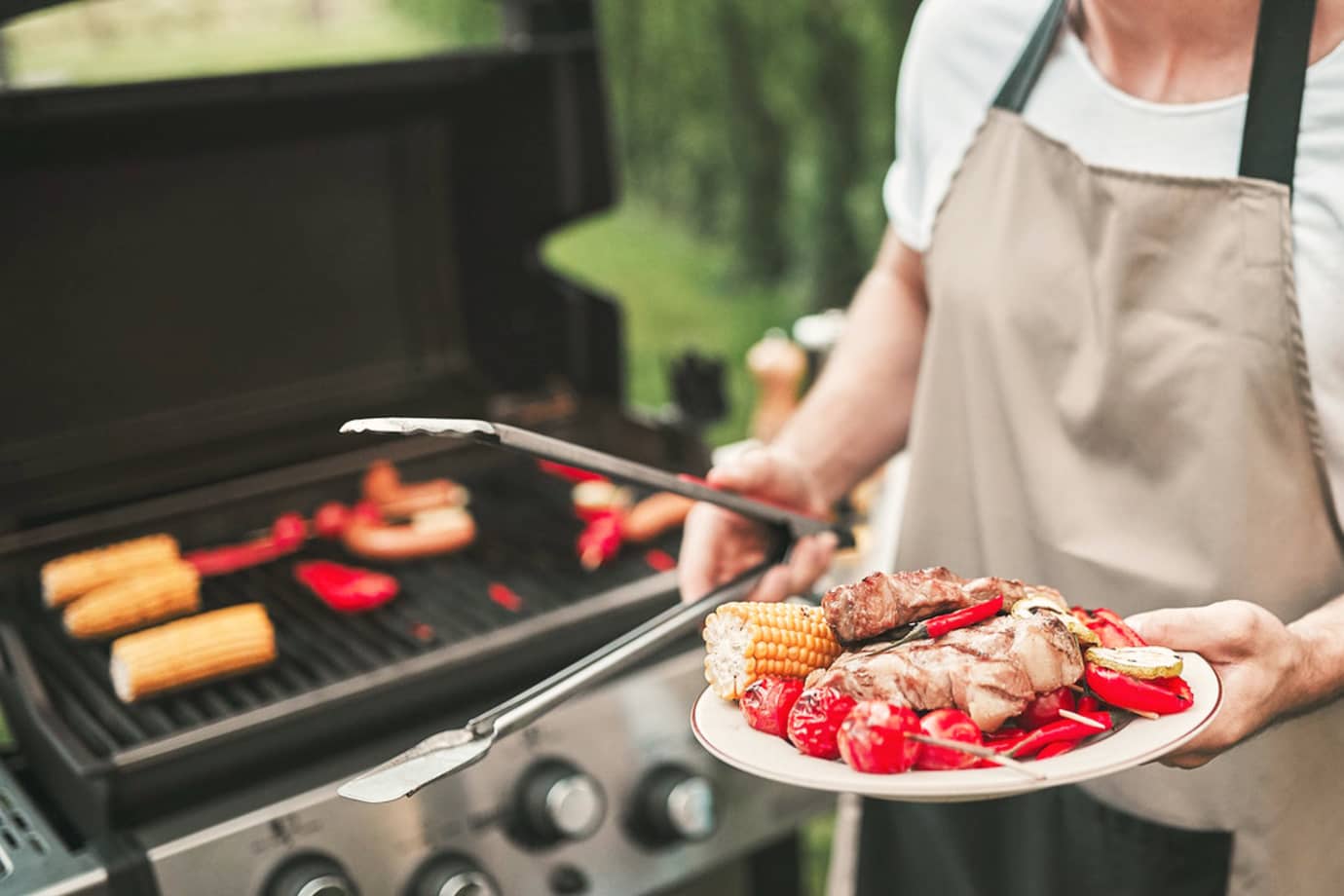 a home chef holds a plate of grilled meat and vegetables in front of a barbecue