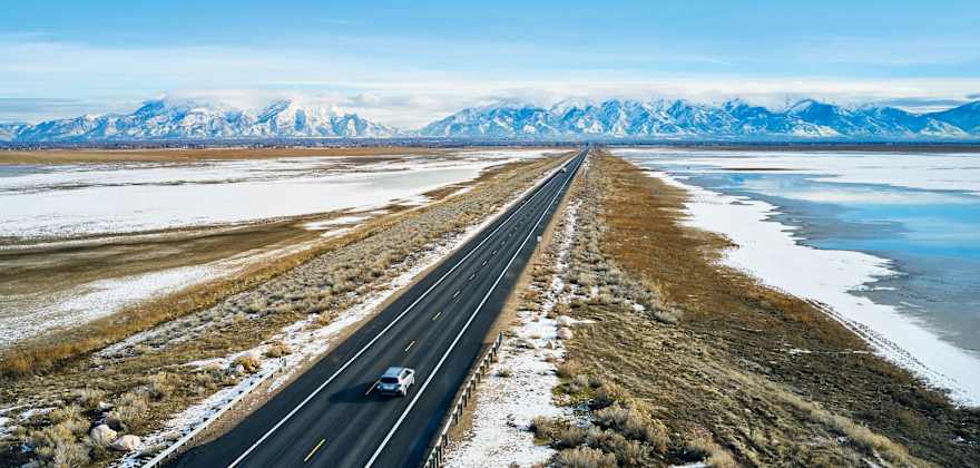 Cars drive on a road surrounded by a dusting of snow.