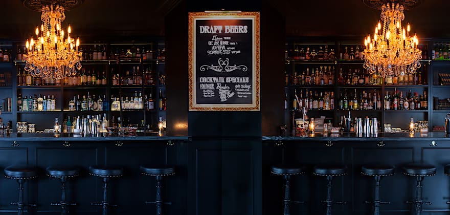 Two chandeliers hang over Death and Taxes ornate black bar, image