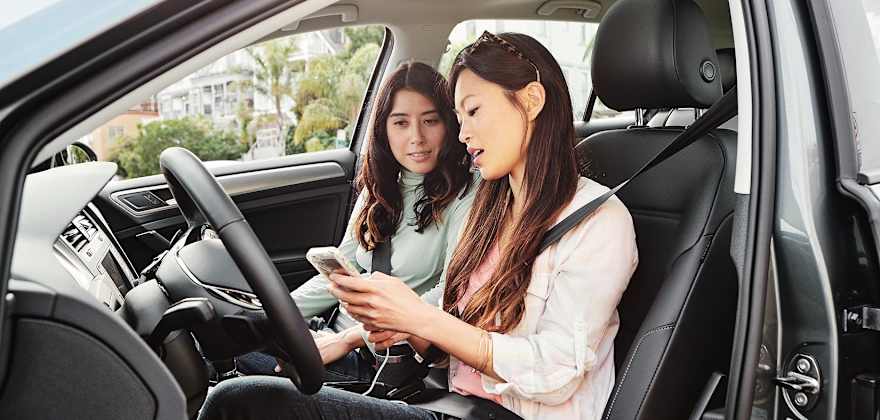 two young women look at a cell phone in a car