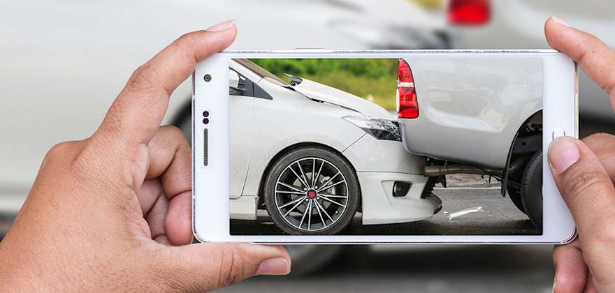 A person's hands on their mobile phone taking a picture of their recent collision for insurance