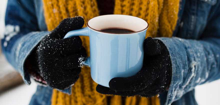 A person holds a blue coffee mug on a snowy morning.