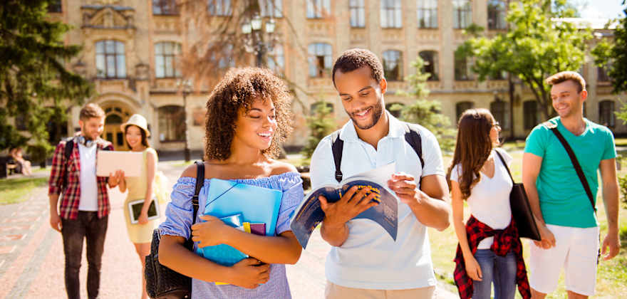 Six college students smile and talk while they walk on campus