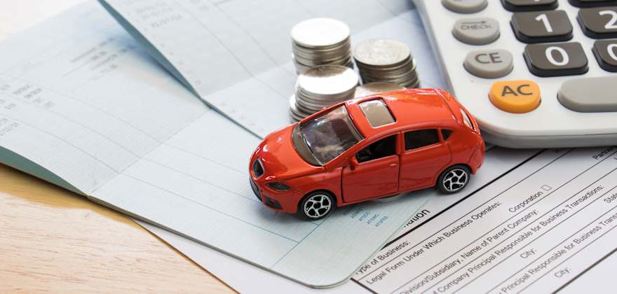 A toy car sits on top of insurance paperwork with stacked coins and a calculator