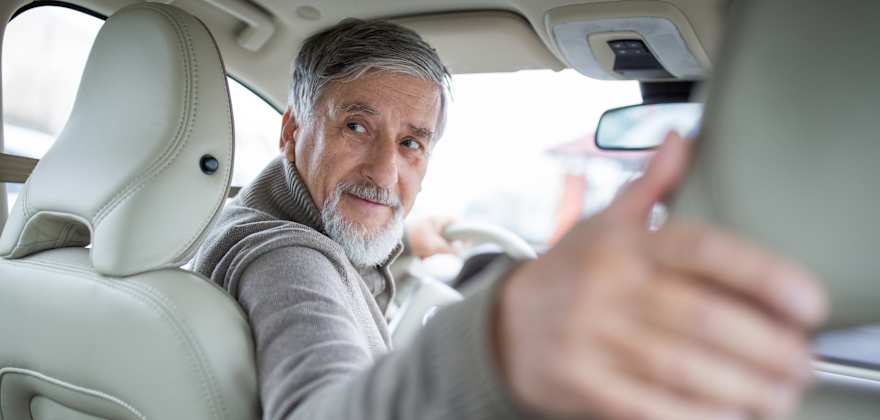 An elderly driver with his head turned to look behind him when backing up