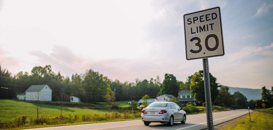 A car drives on a rural road under a 30 mph speed limit sign.