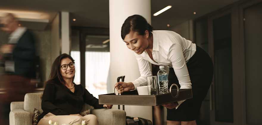 An airport lounge employee sets down a tray of drinks in front of a traveler.