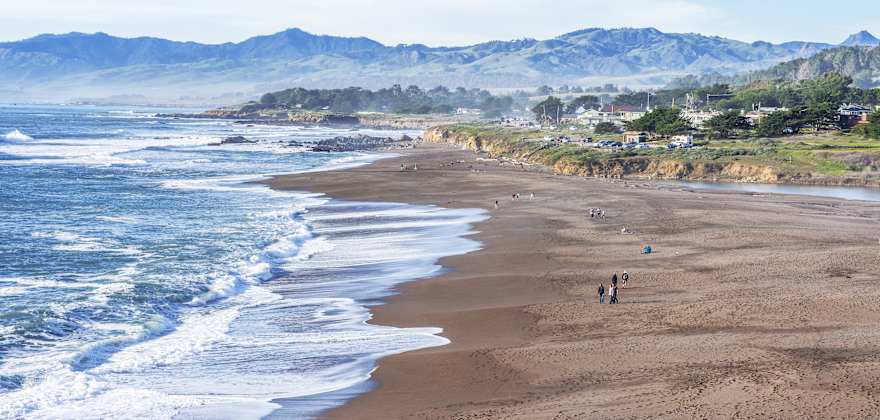 People walk along the sand at Moonstone Beach in Cambria, California.