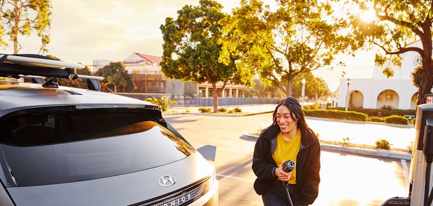 A woman walks an EV charging cable to her Hyundai Ioniq5 EV.