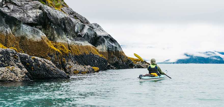 a person kayaks next to a picturesque mountain in Alaska