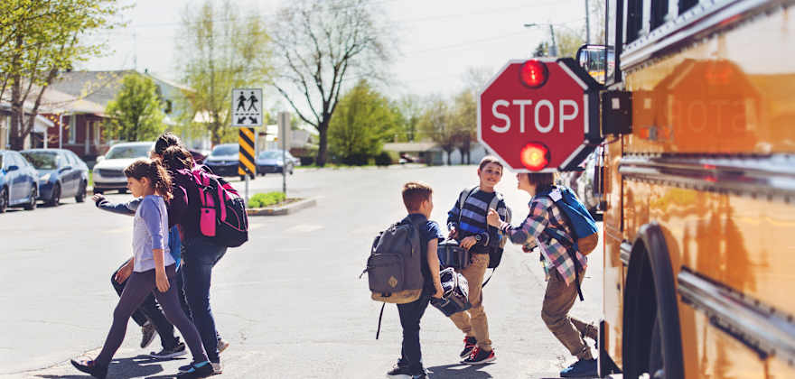 Kids with backpacks step off a school bus