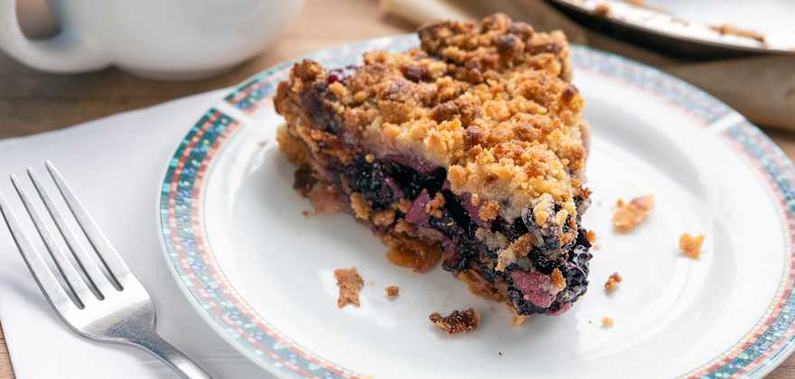 a piece of berry crumble pie on a white plate.