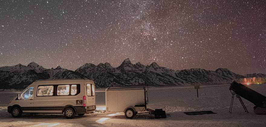 a van is parked near a telescope with a brilliant starry sky and mountains in the distance