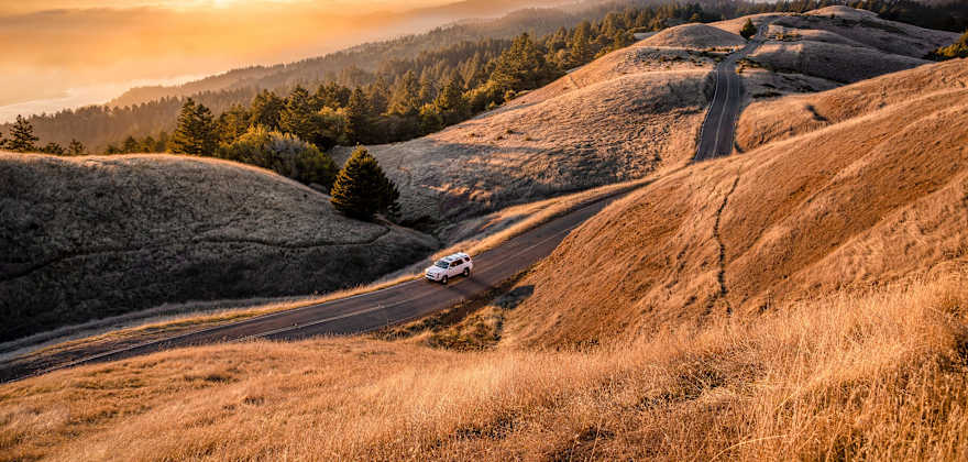 An SUV drives along the golden slopes of Mt. Tamalpais at sunset. 